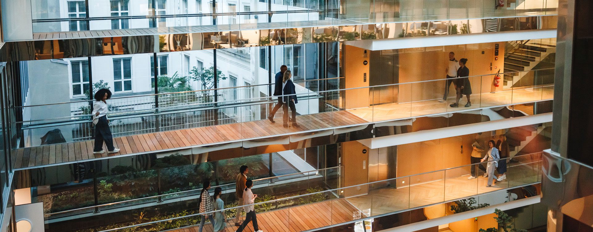Far away shot of people walking across three levels of glass-paneled walkways in a modern office setting