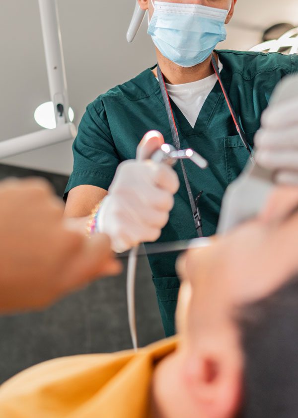 Close up of a masked dentist using a water pick on a patient who is blurred in the foreground
