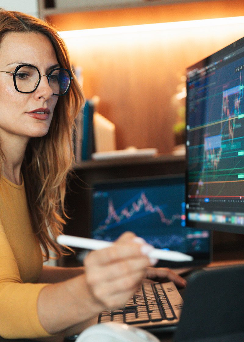 Woman in glasses sits before a computer with charts on it and uses a white stylus