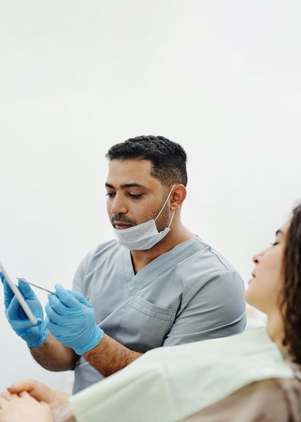 Male dentist with his mask lowered explains something to a female patient in a chair