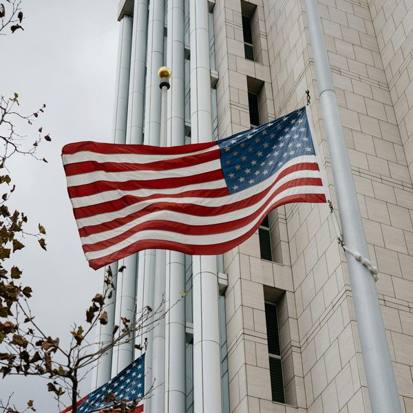 Shot from below, an American flag is hoisted up the flagpole in front of a building