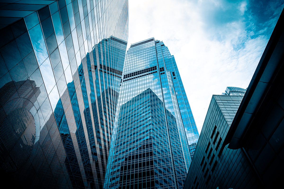 Shot from below, towering reflective skyscrapers rise up towards a cloudy sky
