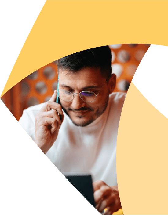 A man wearing glasses and a white shirt talks on a smartphone while looking at a tablet, with yellow geometric shapes framing the image.