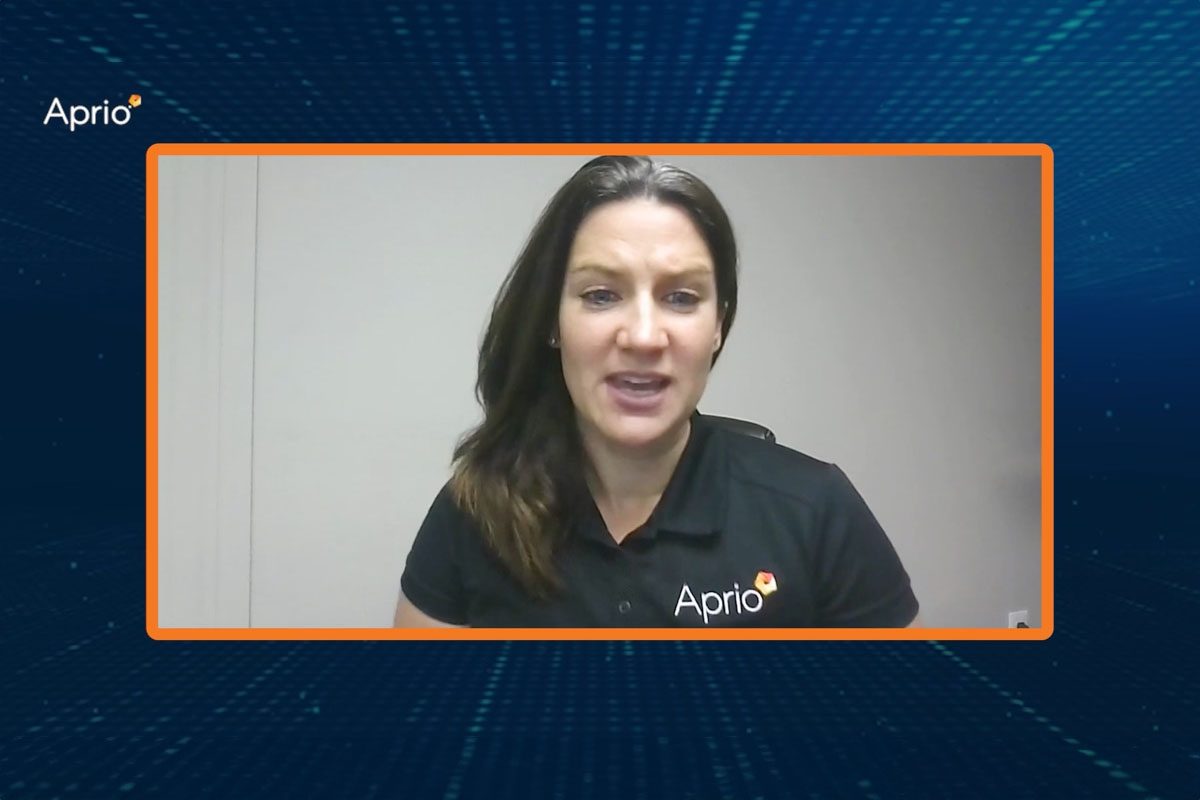 A woman in an Aprio-branded shirt speaks during a video call, framed by a digital blue and orange border with the Aprio logo in the corner.