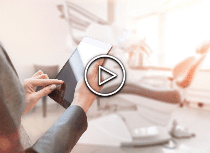 A person uses a tablet in a modern, brightly lit dental office. A large play button icon is overlaid on the image.