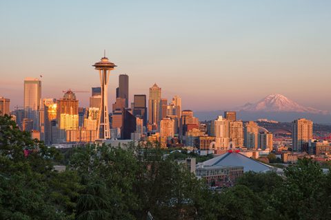 Seattle skyline at sunset with the Space Needle in the foreground, downtown buildings, and Mount Rainier visible in the background.