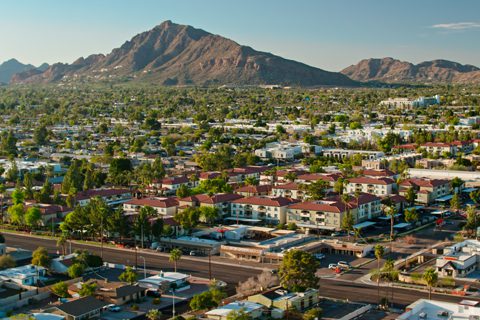 A suburban neighborhood with red-roofed buildings and streets, set against a backdrop of a mountain under a clear blue sky.