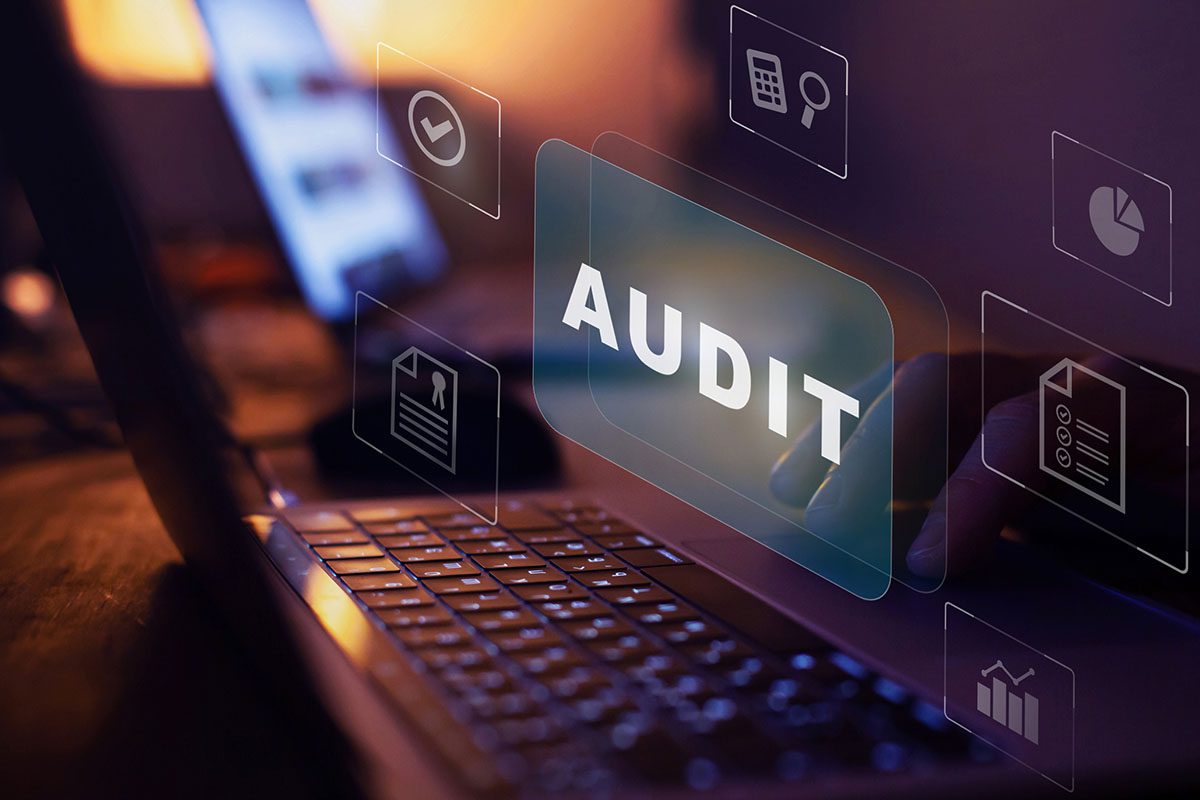 A person works on a laptop with the word AUDIT and various digital business icons displayed on a transparent overlay.