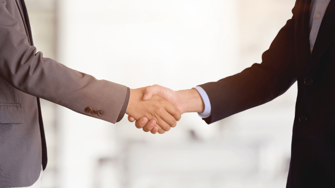 Two people wearing business suits shaking hands in a professional setting, symbolizing agreement or partnership.