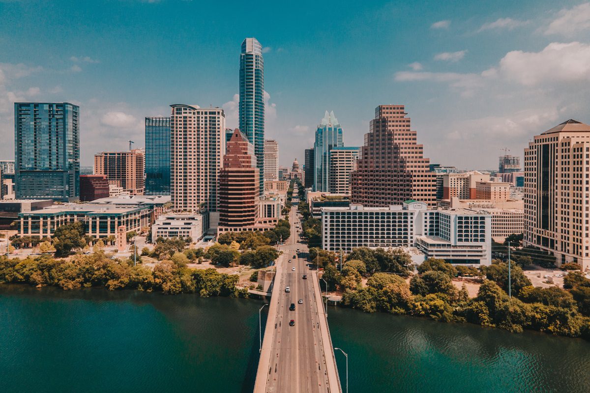Aerial view of downtown Austin, Texas, showing tall buildings, a bridge over the river, and cars driving across.
