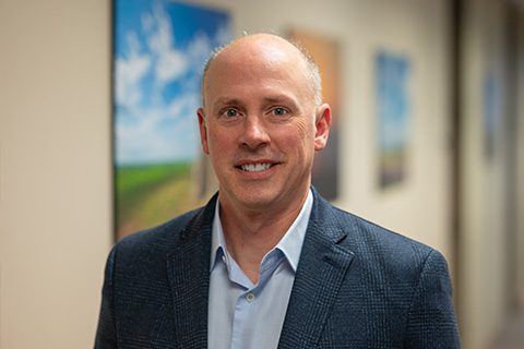 Man in a blazer smiles in a blurred hallway