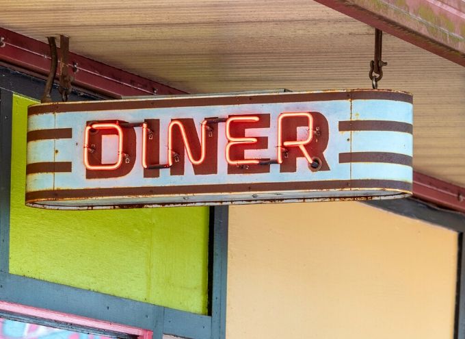 A vintage metal sign with red neon letters spelling Diner is mounted above the entrance of a building with colorful walls.