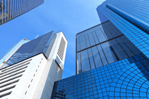 Tall modern skyscrapers with glass and steel facades against a clear blue sky, viewed from below.