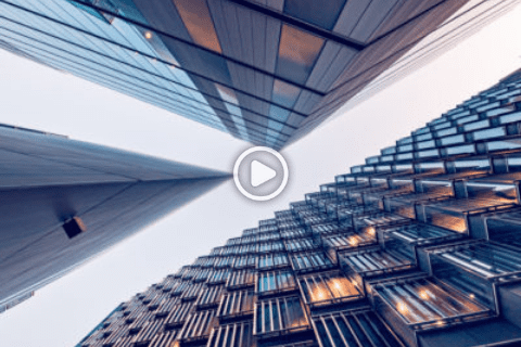 Upward view of three modern skyscrapers with glass and metal facades converging toward the sky, some windows illuminated.