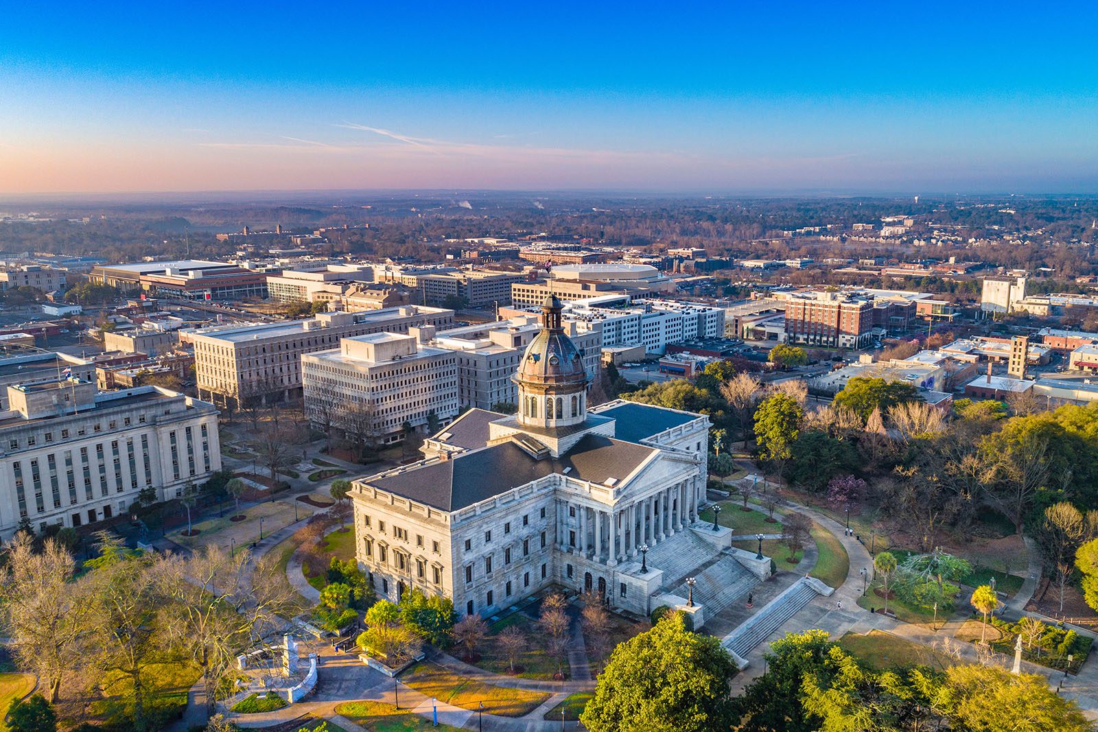Aerial view of the South Carolina State House, a large historic government building with a dome, surrounded by trees and city buildings in Columbia, South Carolina.