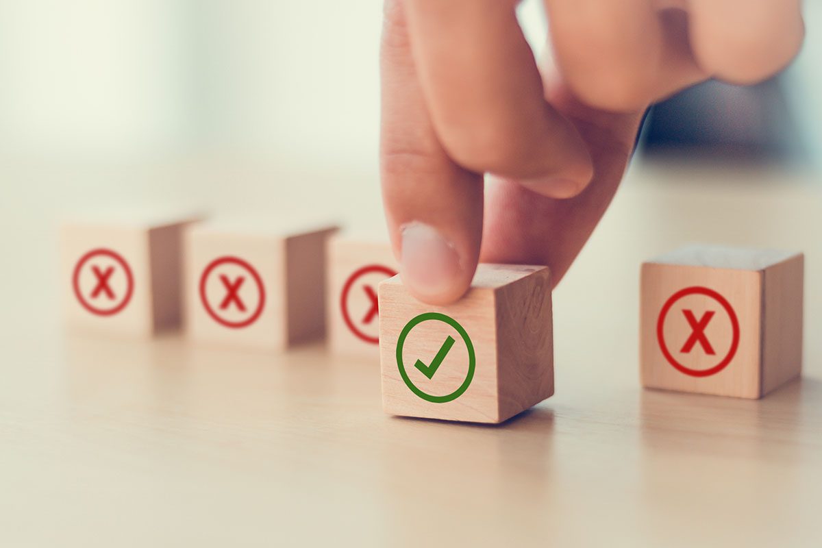 A hand selects a wooden block with a green check mark among blocks with red X marks on a light surface.
