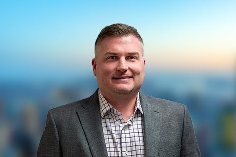 Man in a blazer smiles in front of a bright blurred background
