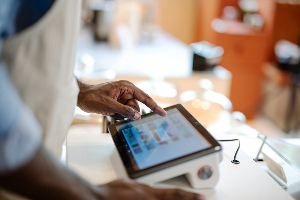 A person uses a touchscreen point-of-sale system at a counter, selecting options on the screen in a well-lit environment.