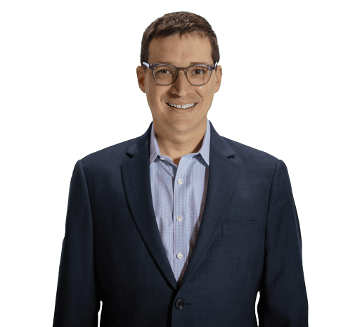 A man wearing glasses and a dark blue suit jacket over a light blue button-up shirt, smiling against a plain white background.