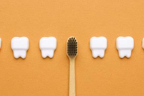 A bamboo toothbrush is placed upright between four white tooth-shaped figures on an orange background.