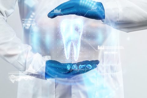 A person in a white lab coat and blue gloves holds their hands around a glowing digital tooth hologram with scientific graphics.