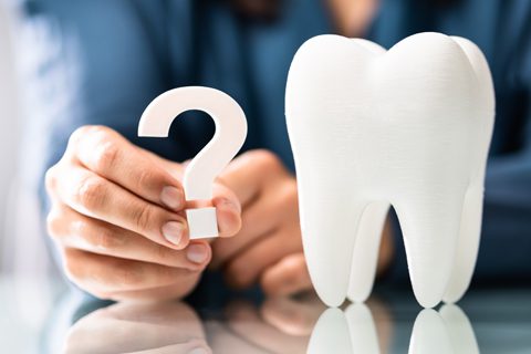 A person holds a white question mark next to a large model of a tooth on a reflective surface.