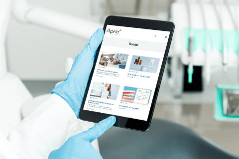A person wearing blue gloves holds a tablet displaying a dental website in a dental clinic setting.