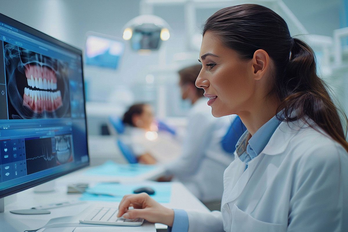 A dentist examines a dental X-ray on a computer screen in a modern clinic, with a patient seated in the background.