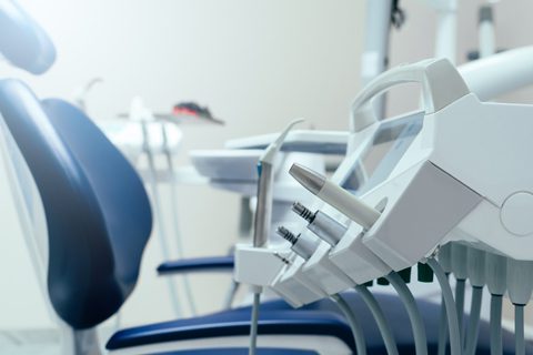 Close-up of dental equipment and instruments next to a blue dental chair in a modern dental clinic.