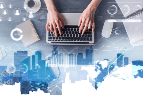 Hands typing on a laptop with a notebook, coffee cup, and digital business graphics overlayed on a cityscape background.