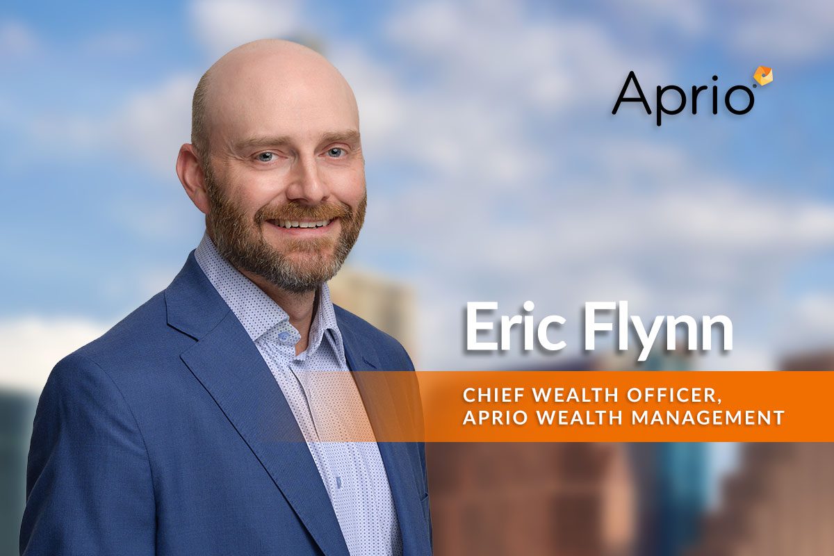 A man in a blue suit smiles in front of a cityscape background, with text identifying him as Eric Flynn, Chief Wealth Officer at Aprio Wealth Management.