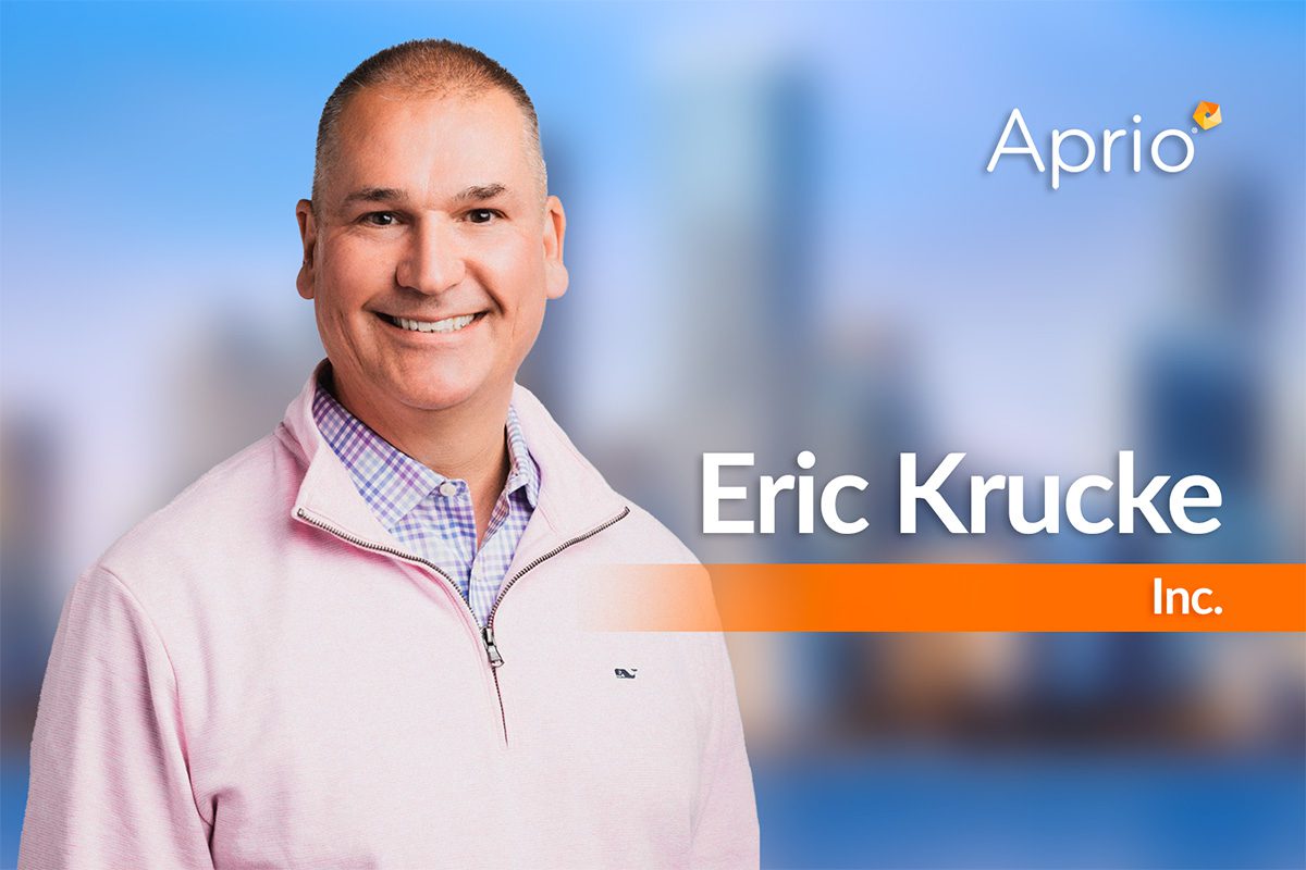 A man in a light pink sweater smiles at the camera, with the text Eric Krucke Inc. and the Aprio logo over a blurred cityscape background.