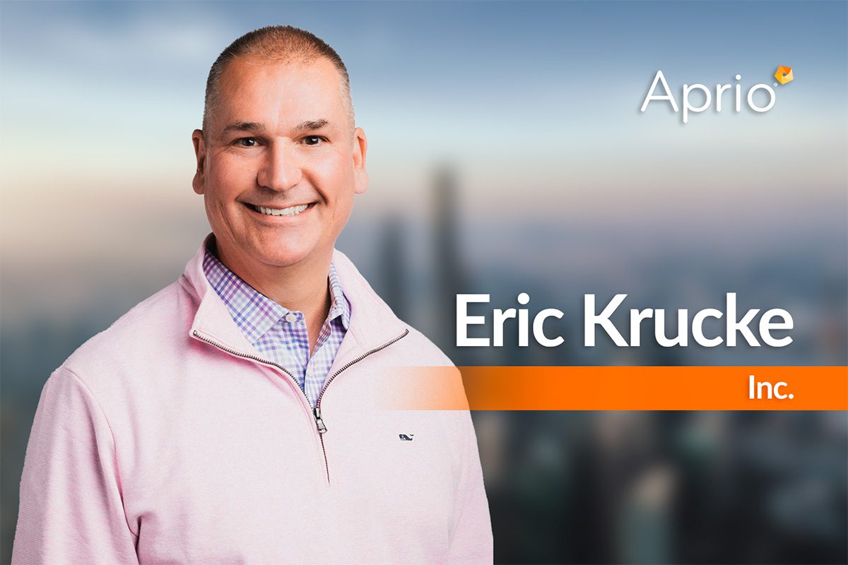 A smiling man in a pink pullover stands in front of a blurred cityscape background with the text “Aprio,” “Eric Krucke,” and “Inc.” displayed.