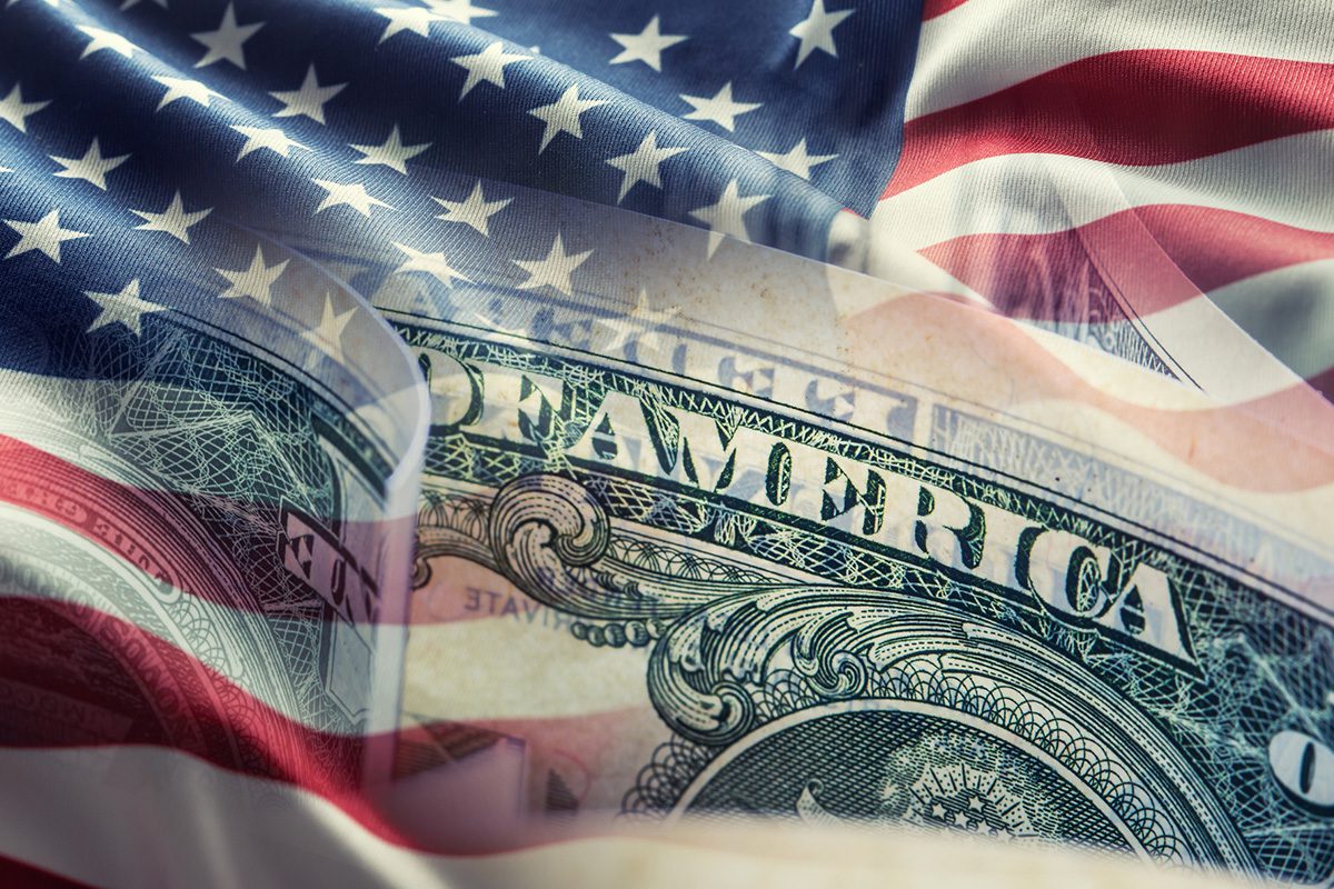 Close-up of a U.S. one-dollar bill overlaid with an American flag, symbolizing the relationship between the United States and its currency.
