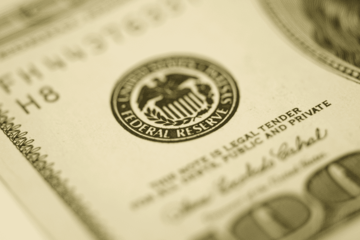 Close-up of the Federal Reserve System seal and part of the serial number on a U.S. dollar bill, shown in a yellowish tone.