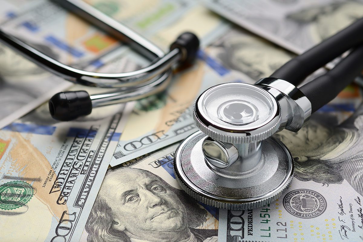 A stethoscope resting on several US hundred dollar bills, symbolizing the relationship between healthcare and money.