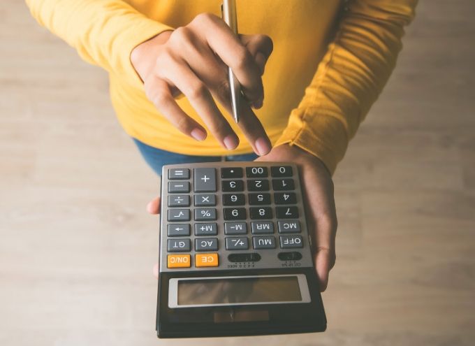 A person in a yellow shirt holds a calculator and presses a button with a pen.