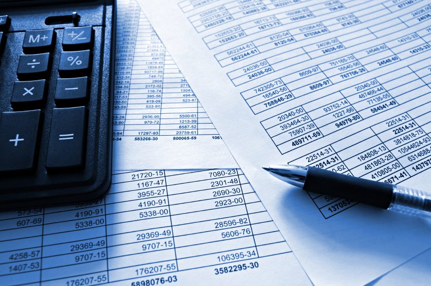 A close-up of a calculator, a pen, and printed spreadsheets filled with numbers and financial data.