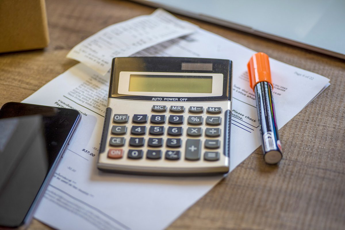 A calculator, a document, an orange marker, and a smartphone are placed on a wooden desk.