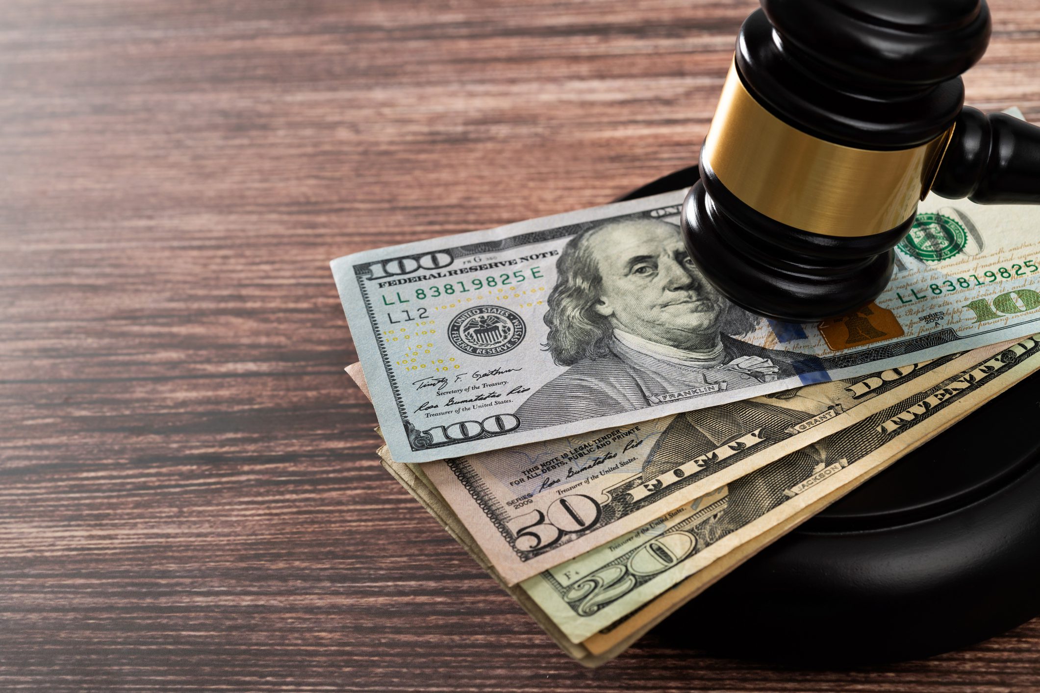 A gavel rests on top of several U.S. dollar bills, including $100, $50, and $20 notes, on a wooden surface.