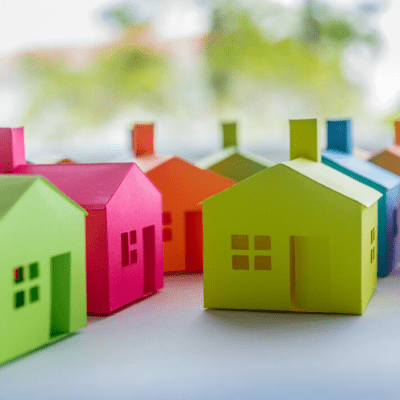 Several colorful paper houses are arranged on a flat surface with a blurred green background.