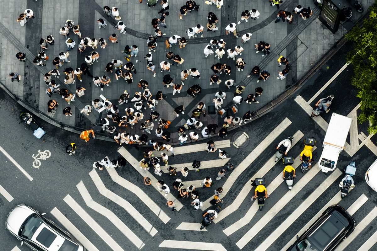 Aerial view of a crowded crosswalk and sidewalk, with people waiting to cross the street and several vehicles stopped at the intersection.