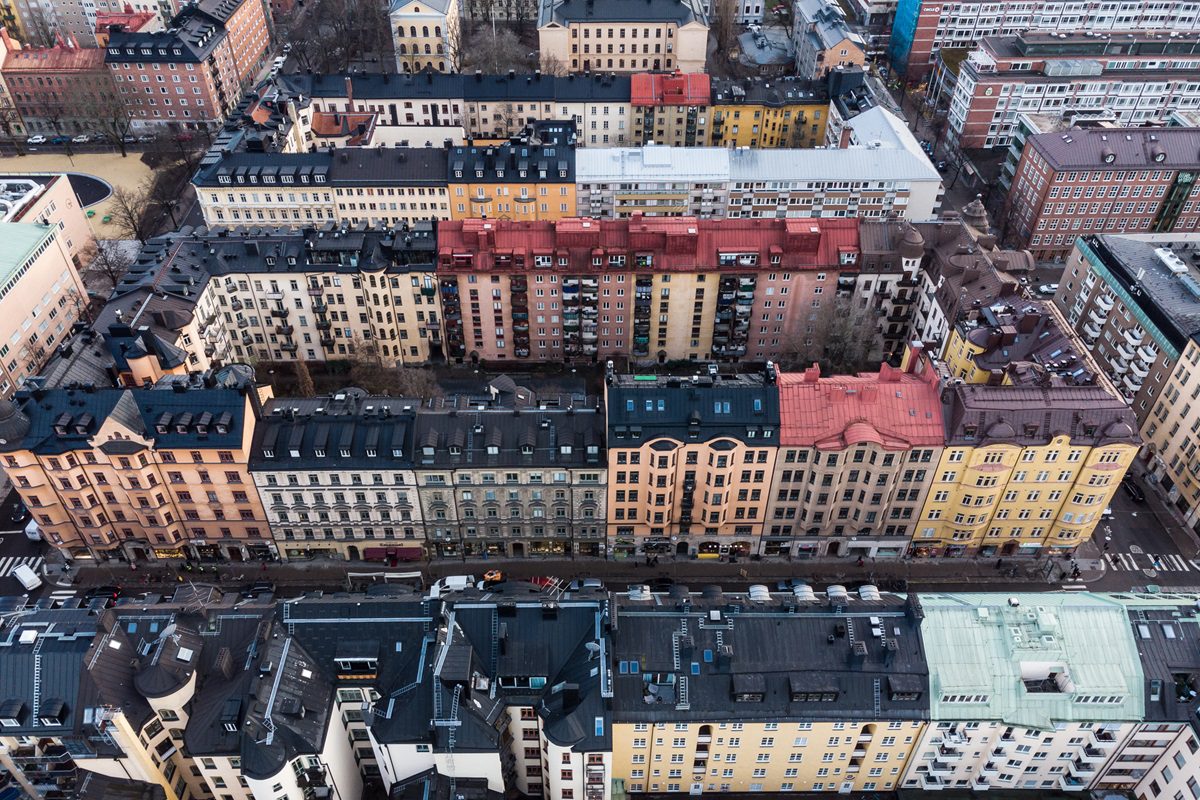Aerial view of a city block with multi-story residential buildings in various colors, parked cars along the street, and some trees visible.