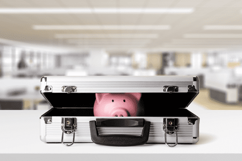 A pink piggy bank partially visible inside an open silver briefcase on a white desk in an office setting.