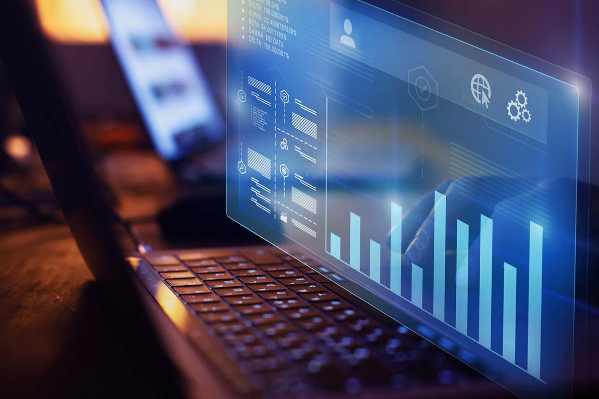 A close-up of a laptop displaying digital graphs and data visualizations on a transparent screen, with a blurred background.