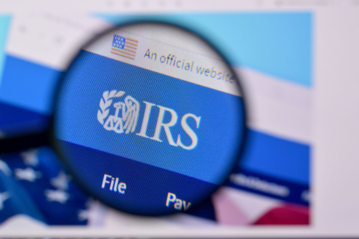 A magnifying glass focuses on the IRS logo and website header, showing the phrase An official website and part of the navigation menu.