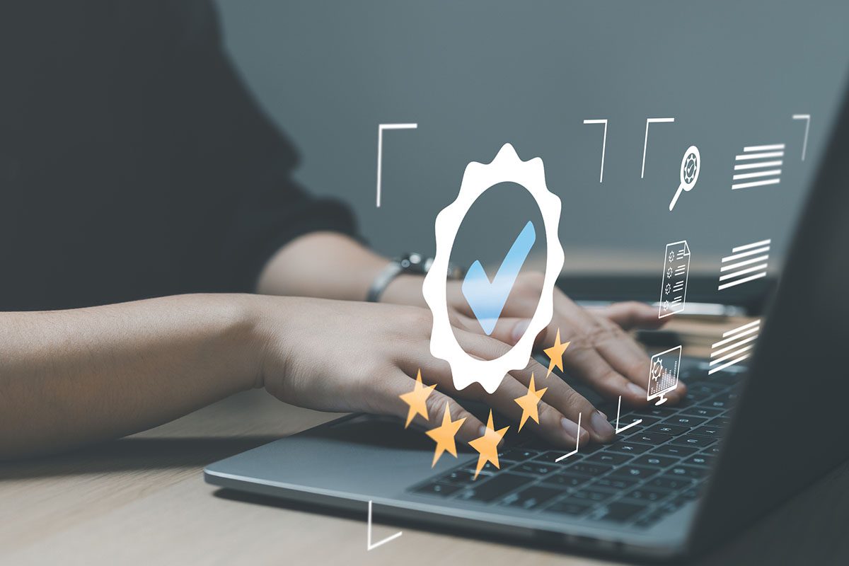 Hands typing on a laptop with digital icons overlayed, including a checkmark in a badge and five stars, representing quality assurance or online certification.