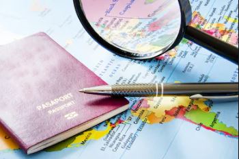 A passport, pen, and magnifying glass rest on a colorful map, suggesting themes of travel, planning, and exploration.