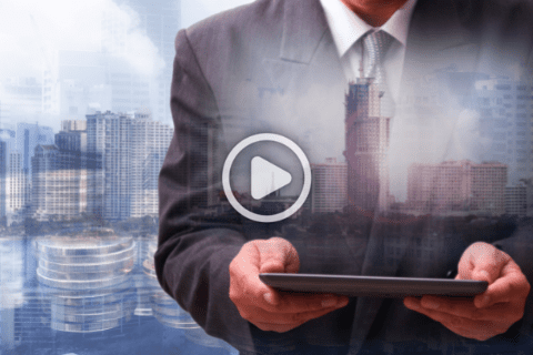 A man in a suit holds a tablet, with a cityscape and a play button icon superimposed, suggesting a business-related video.