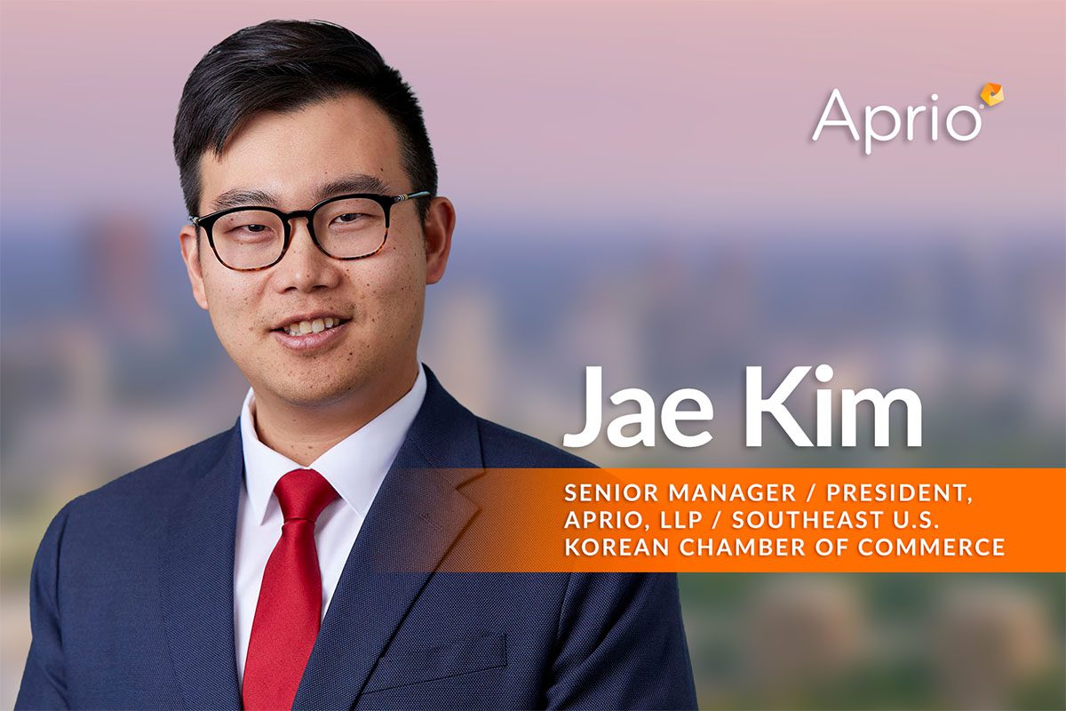 A man in a suit and red tie stands in front of a blurred cityscape background. Text next to him reads Jae Kim, Senior Manager / President, Aprio LLP / Southeast U.S. Korean Chamber of Commerce.
